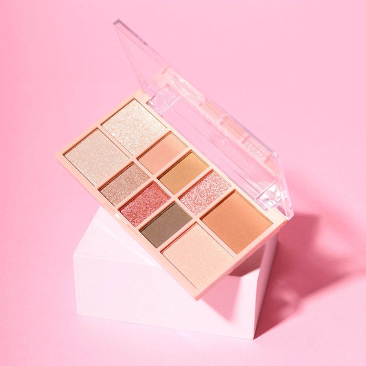 An open 10-shade eyeshadow palette in a peach-toned case, displayed on a white geometric pedestal against a solid pink background.