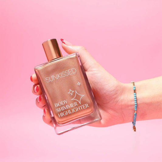 Hand holding a bottle of Sunkissed Body Shimmer Highlighter to demonstrate the liquid gold glow on a pink background