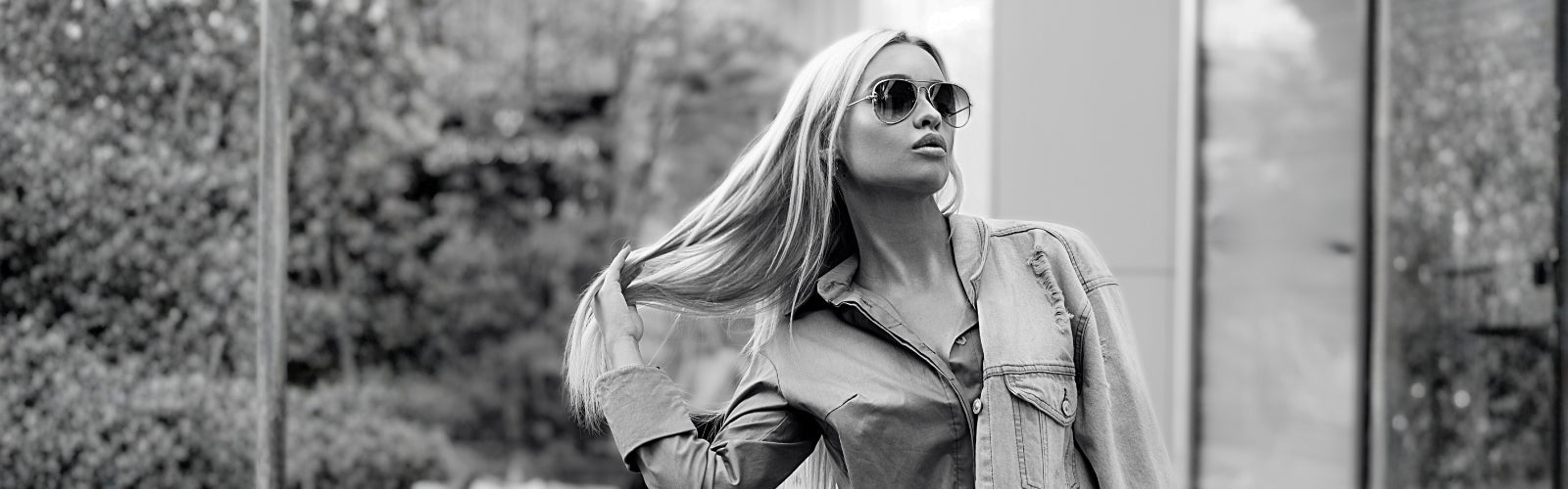 Model with long sleek blonde hair wearing aviator sunglasses in a black and white urban lifestyle banner