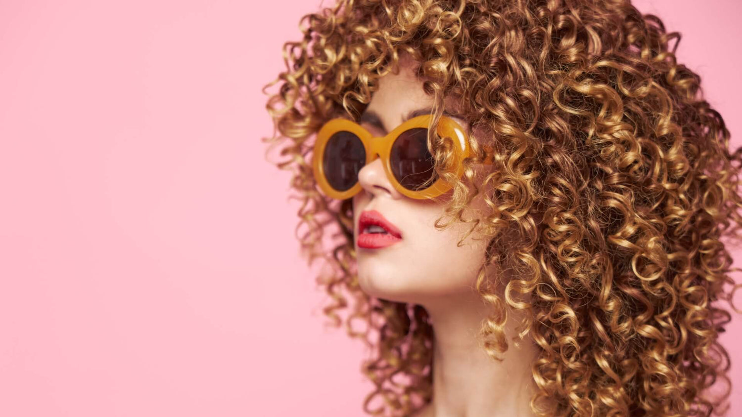 Model with voluminous defined blonde curls and yellow sunglasses showcasing professional hair styling results