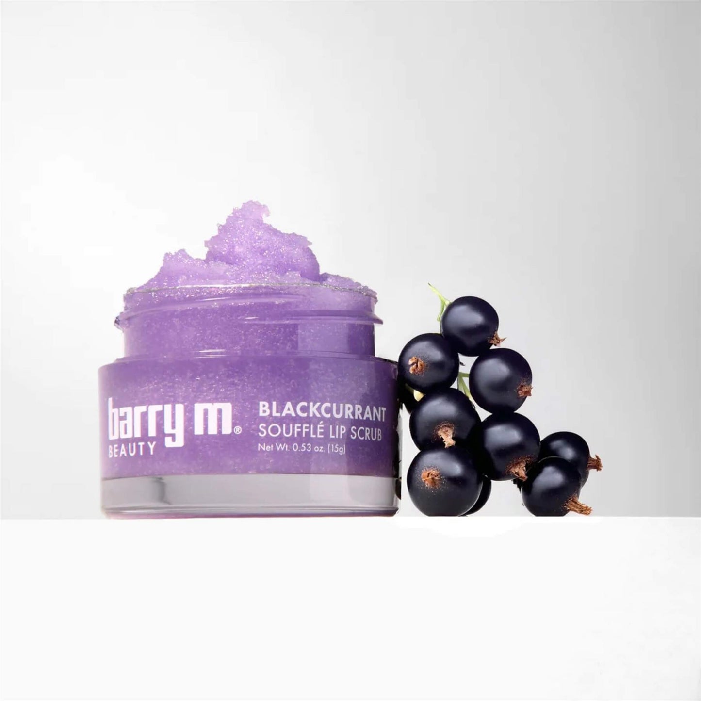 Barry M Blackcurrant Soufflé Lip Scrub 15g jar with purple sugar scrub texture and a cluster of fresh blackcurrants