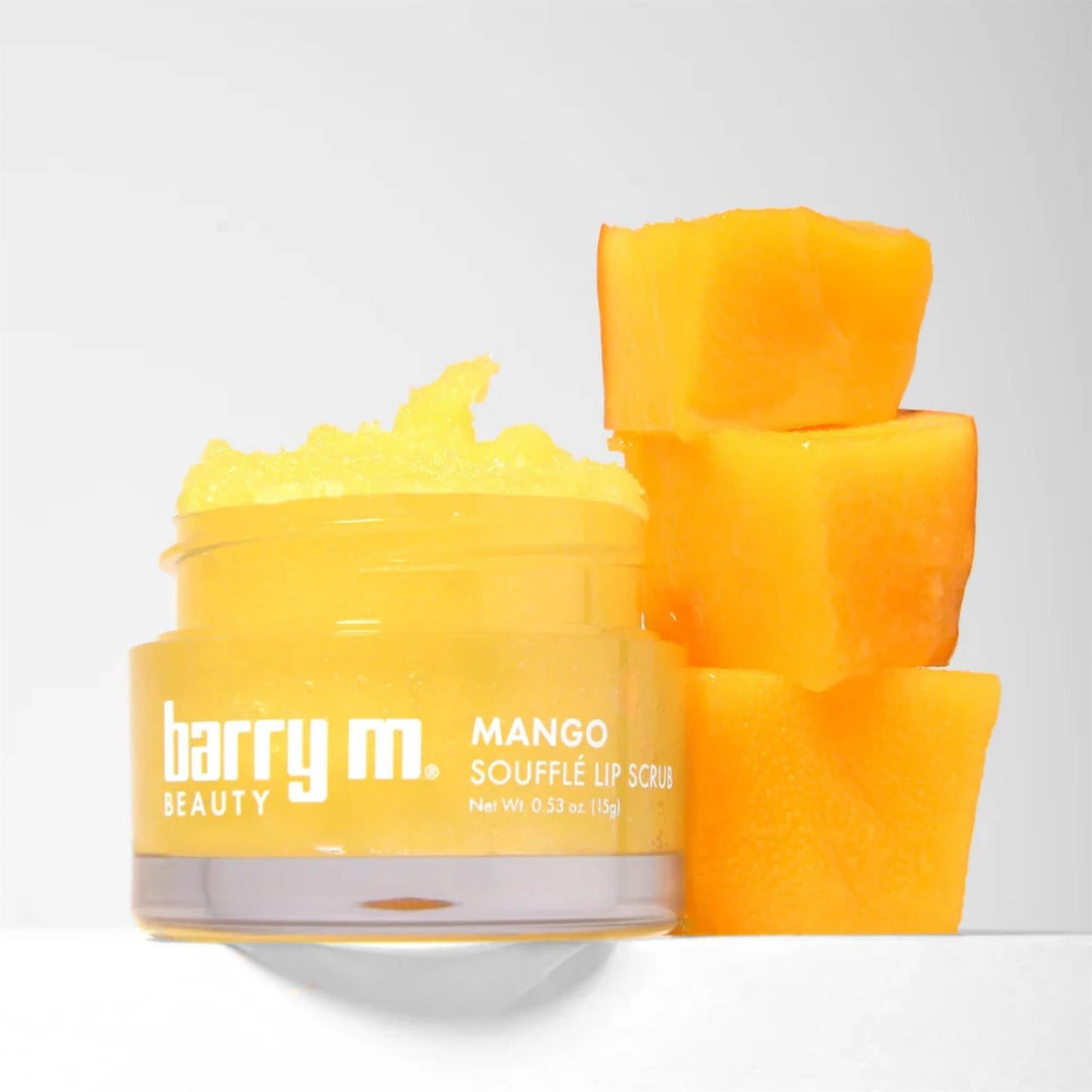 Barry M Mango Soufflé Lip Scrub 15g jar with yellow sugar scrub texture and a stack of fresh mango cubes