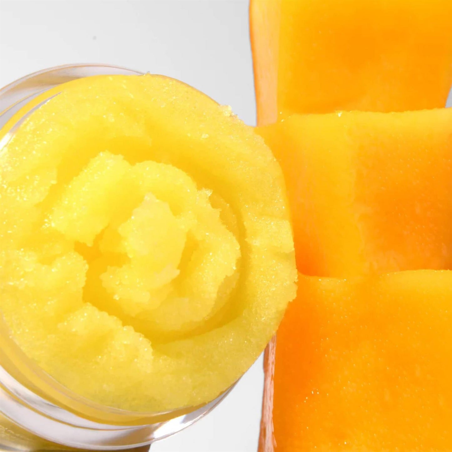 Close-up of Barry M Mango Soufflé Lip Scrub showing the swirled yellow sugary texture next to fresh mango cubes
