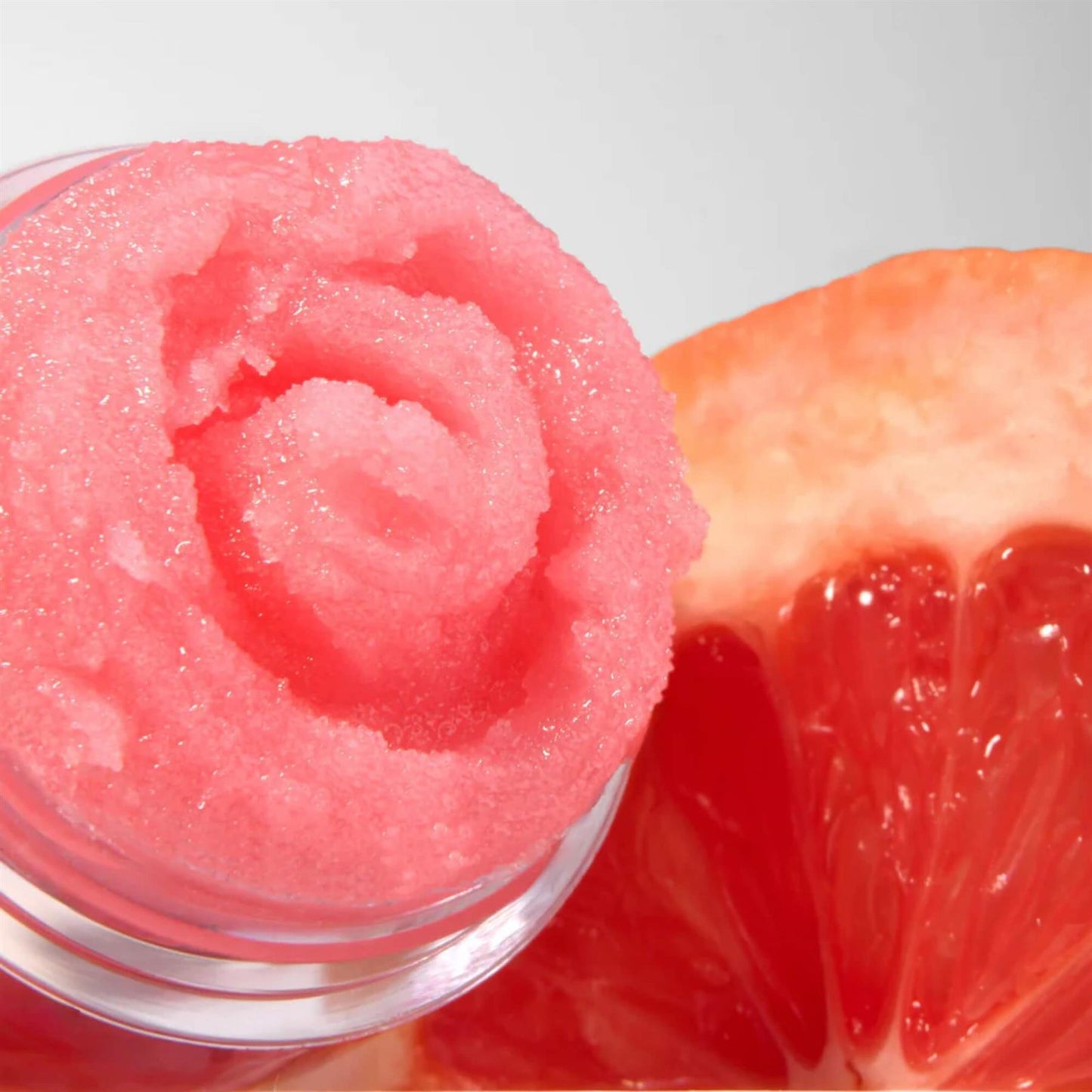 Close-up of Barry M Pink Grapefruit Soufflé Lip Scrub showing the swirled coral pink sugary texture next to a fresh grapefruit slice