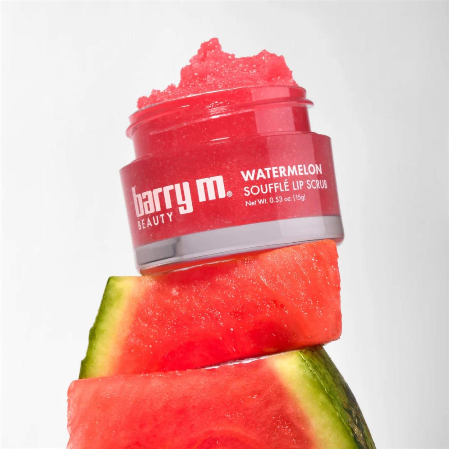Barry M Watermelon Soufflé Lip Scrub 15g jar with red sugar scrub texture stacked on fresh watermelon slices