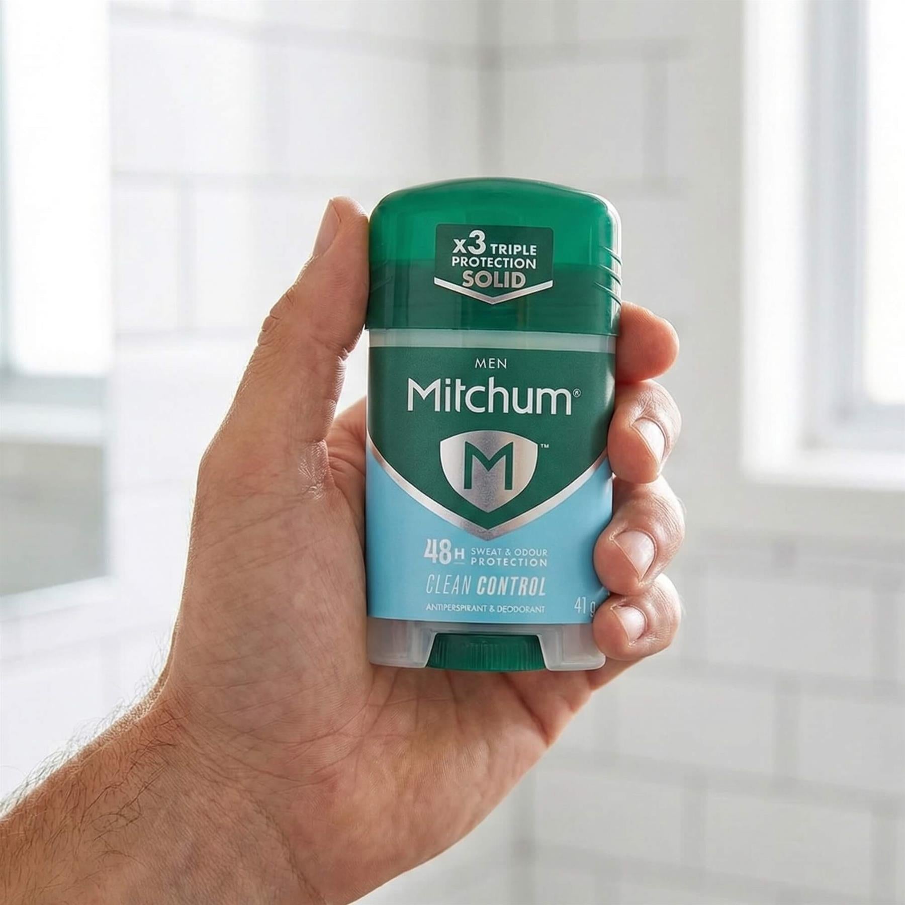 Hand holding Mitchum Men Clean Control 48H Triple Protection antiperspirant solid stick in bathroom