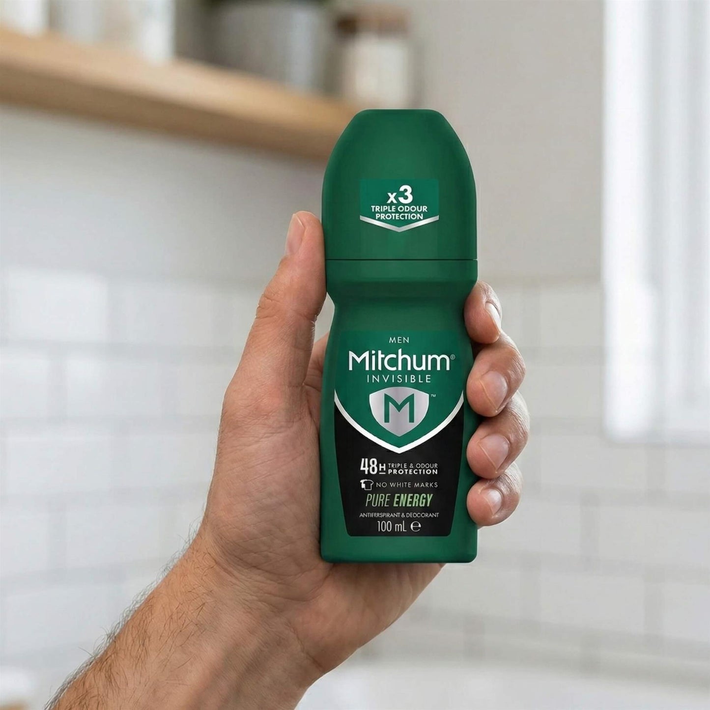 Hand holding Mitchum Men Invisible Pure Energy 48H Triple Odour Protection roll-on in bathroom