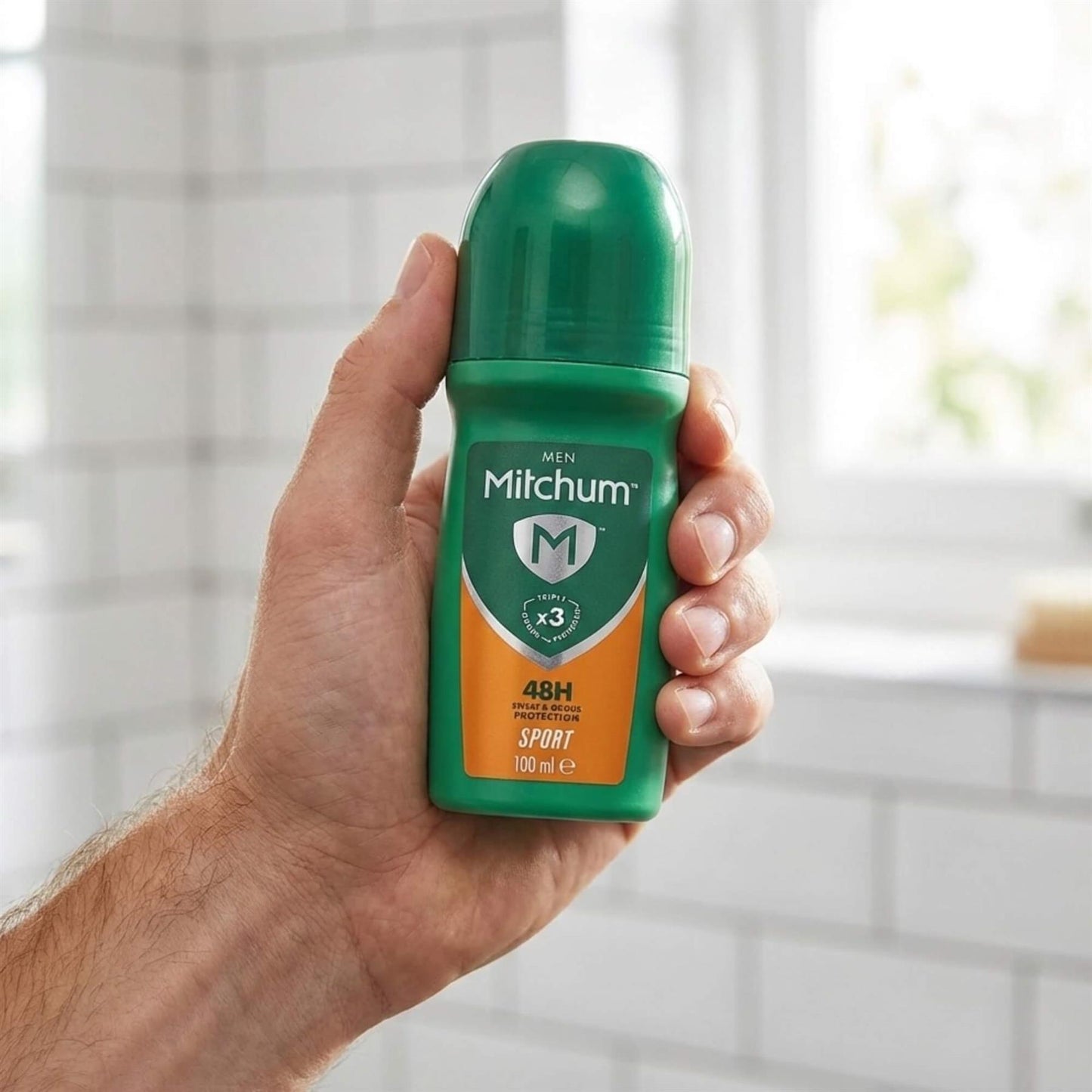 Hand holding Mitchum Men Sport 48H Triple Odour Protection antiperspirant roll-on in bathroom