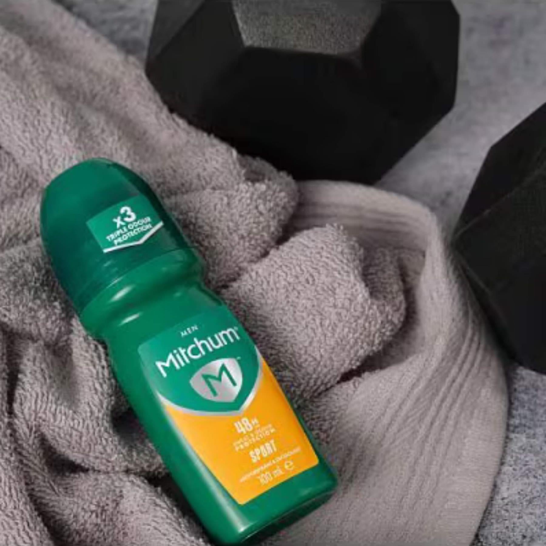 Mitchum Men Sport 48H antiperspirant roll-on in gym bag setting with dumbbells and towel