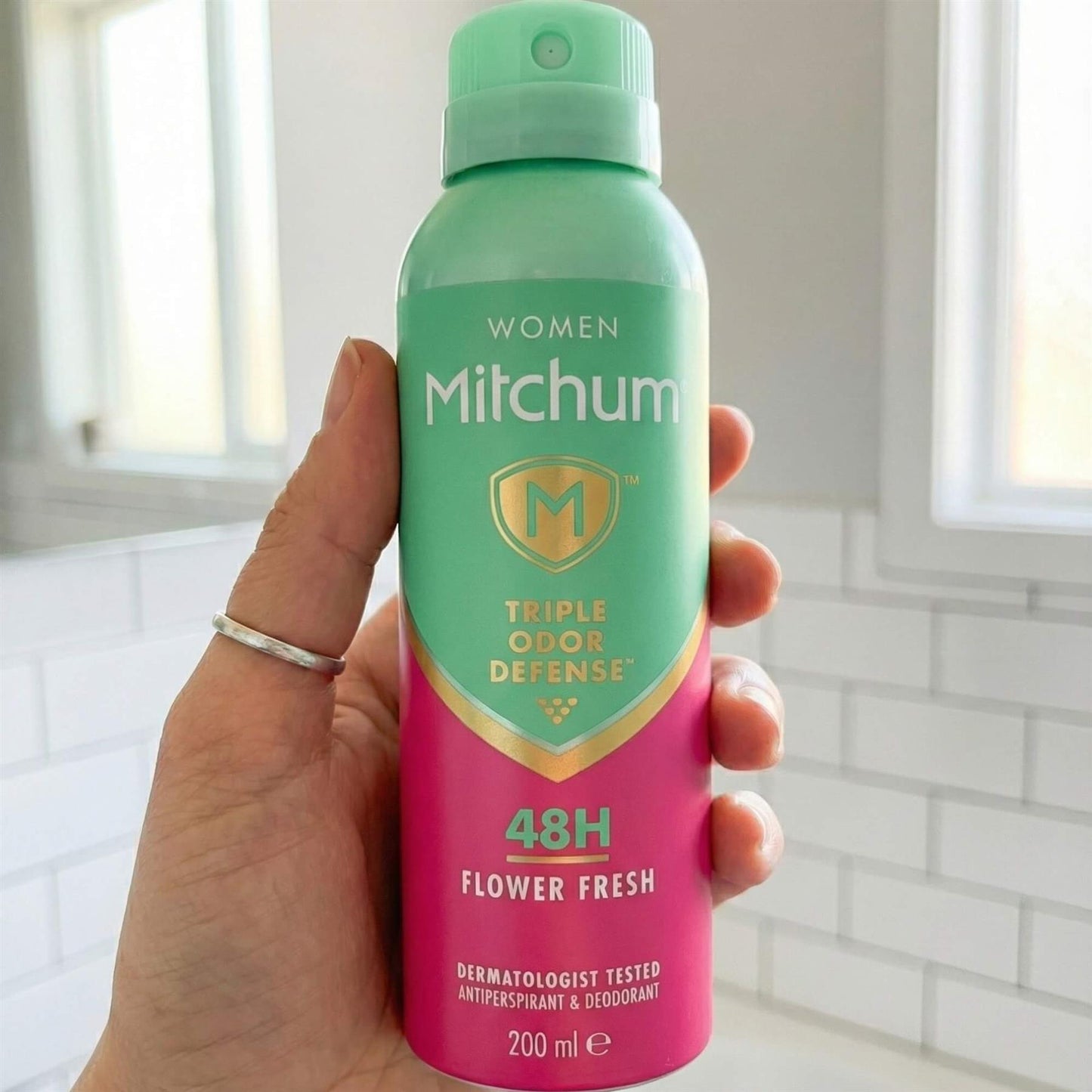 Hand holding Mitchum Women Flower Fresh 48H Triple Odour Defense antiperspirant spray in bathroom