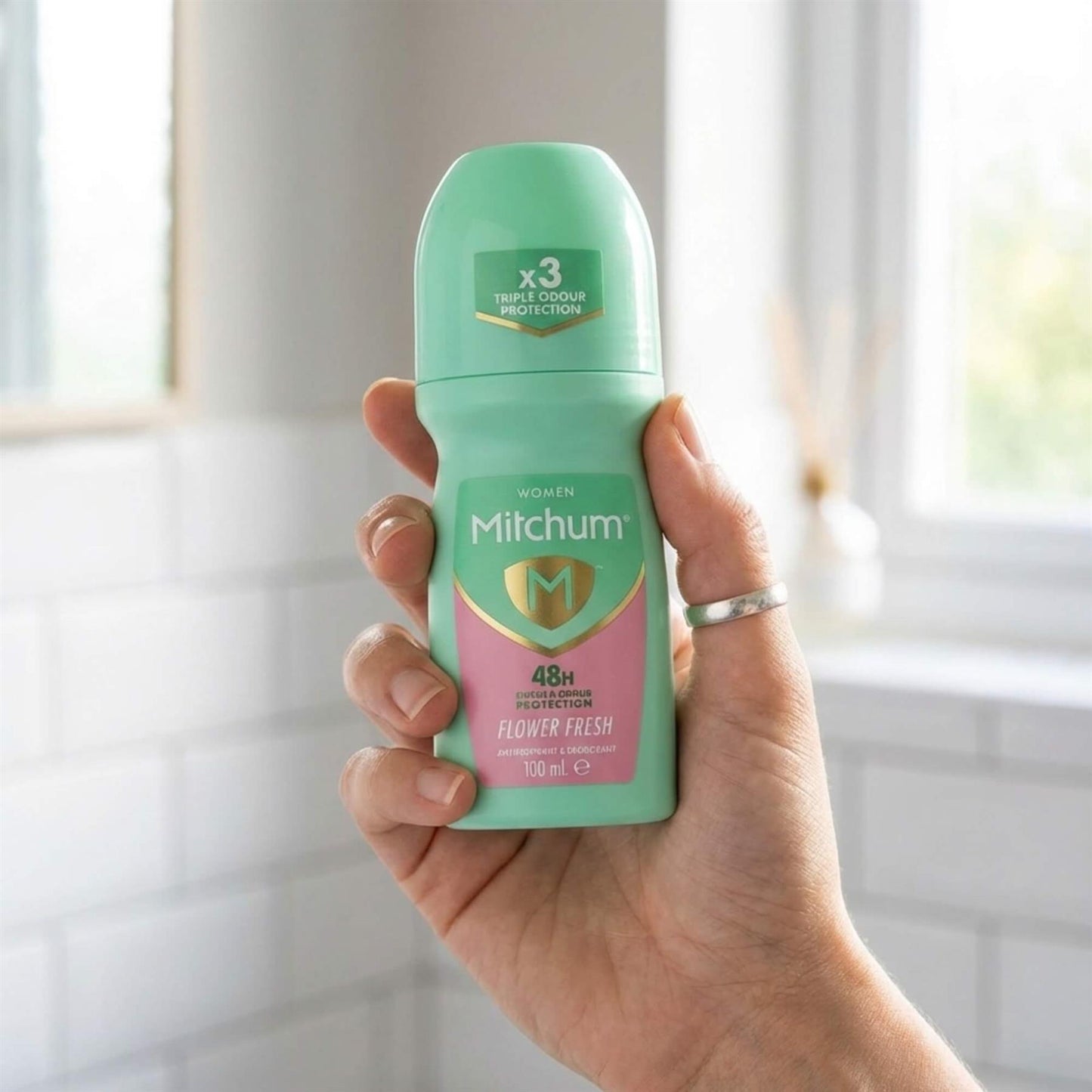 Hand holding Mitchum Women Flower Fresh 48H roll-on 100ml in bright bathroom