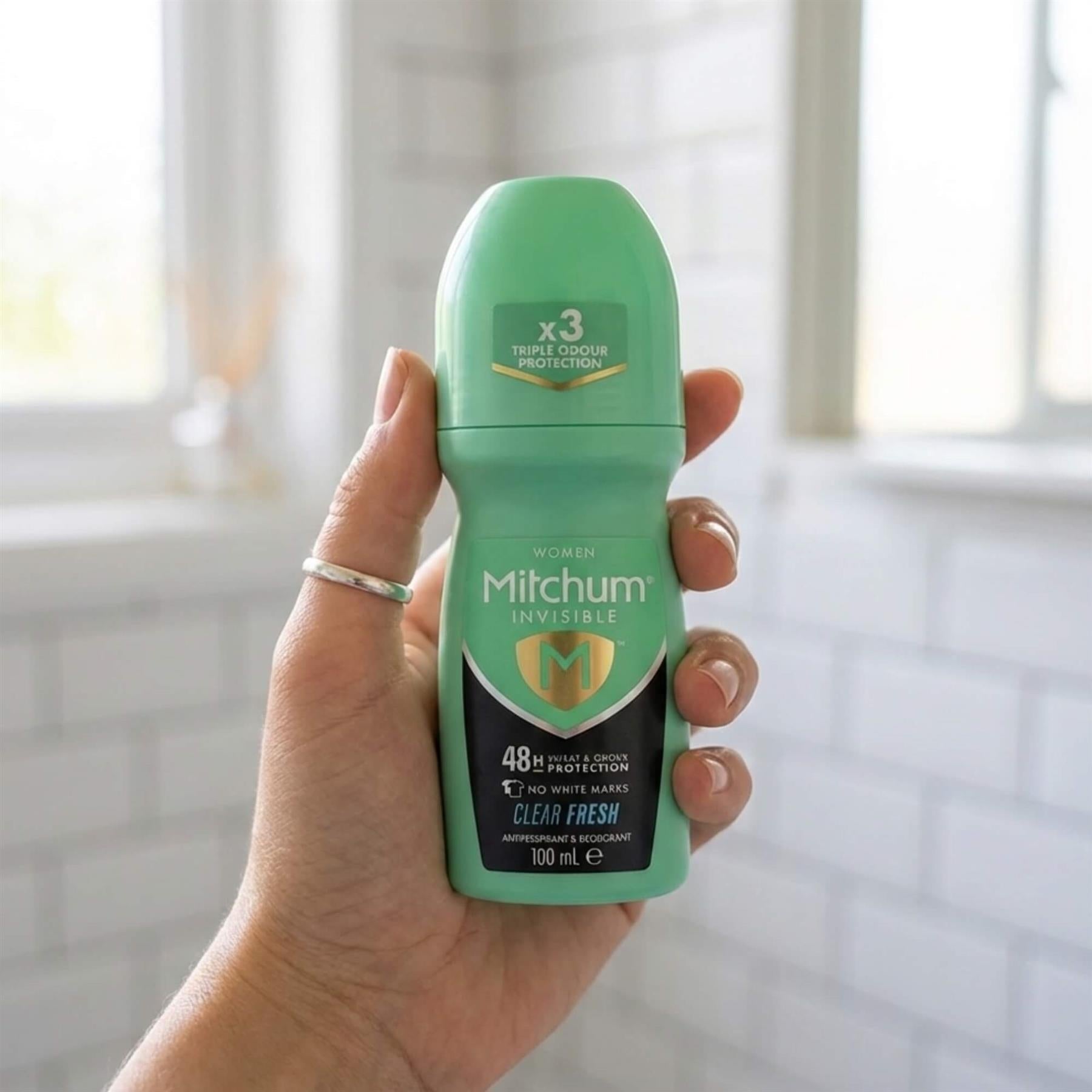 Hand holding Mitchum Women Invisible Clear Fresh 48H antiperspirant roll-on in bathroom