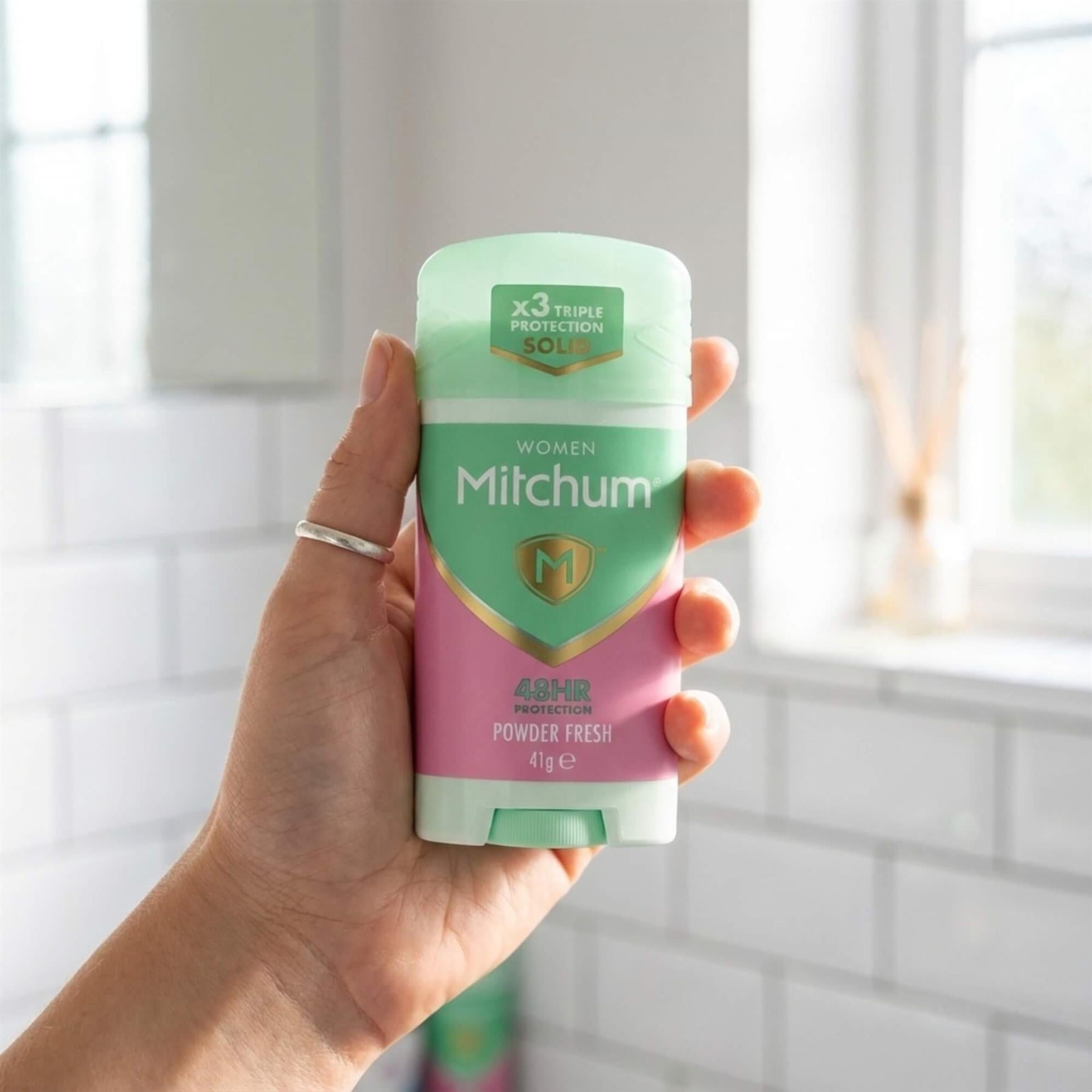 Hand holding Mitchum Women Powder Fresh 48H antiperspirant solid stick 41g in bathroom