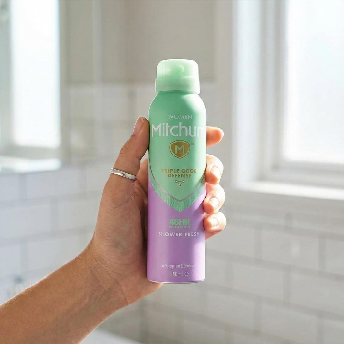 Hand holding Mitchum Women Shower Fresh 48HR Triple Odor Defense antiperspirant spray in bathroom