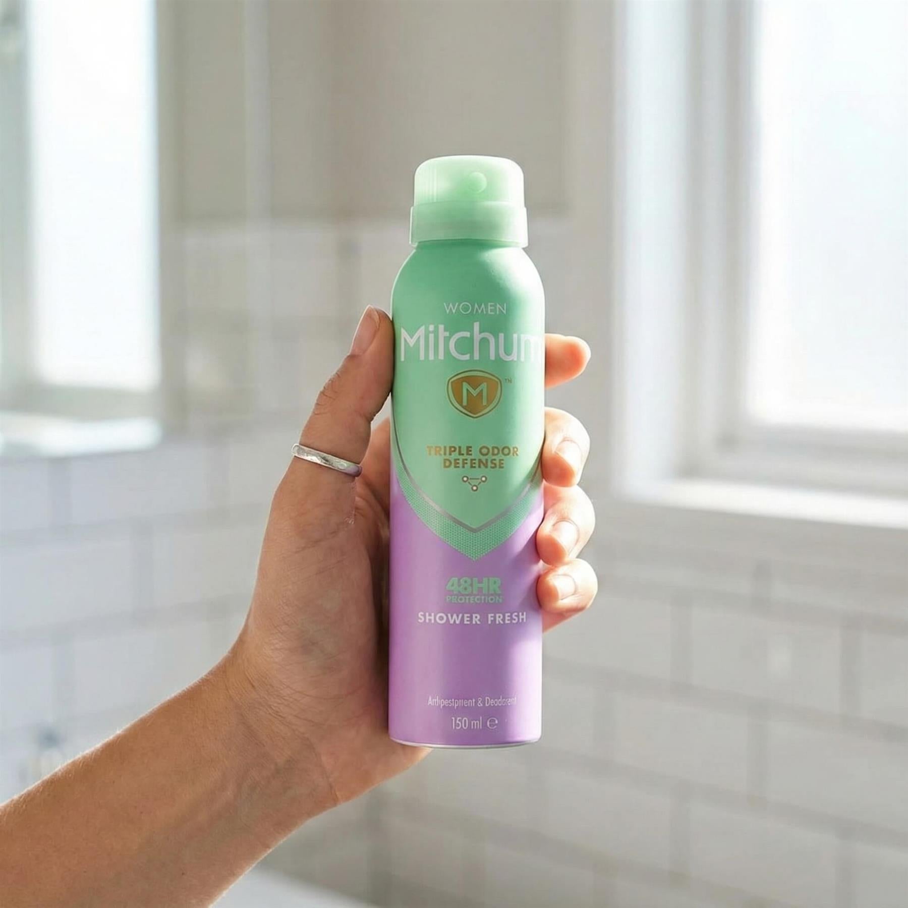 Hand holding Mitchum Women Shower Fresh 48HR Triple Odor Defense antiperspirant spray in bathroom