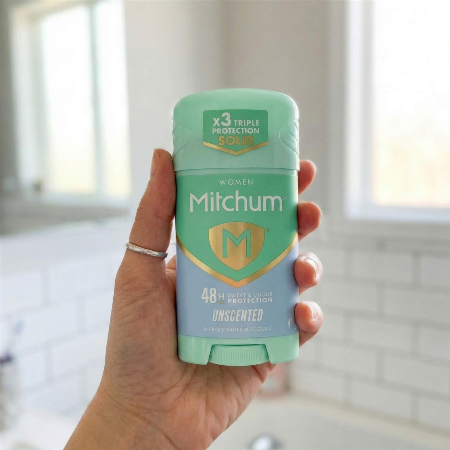 Hand holding Mitchum Women Unscented 48H Triple Odour Protection antiperspirant solid stick in bathroom