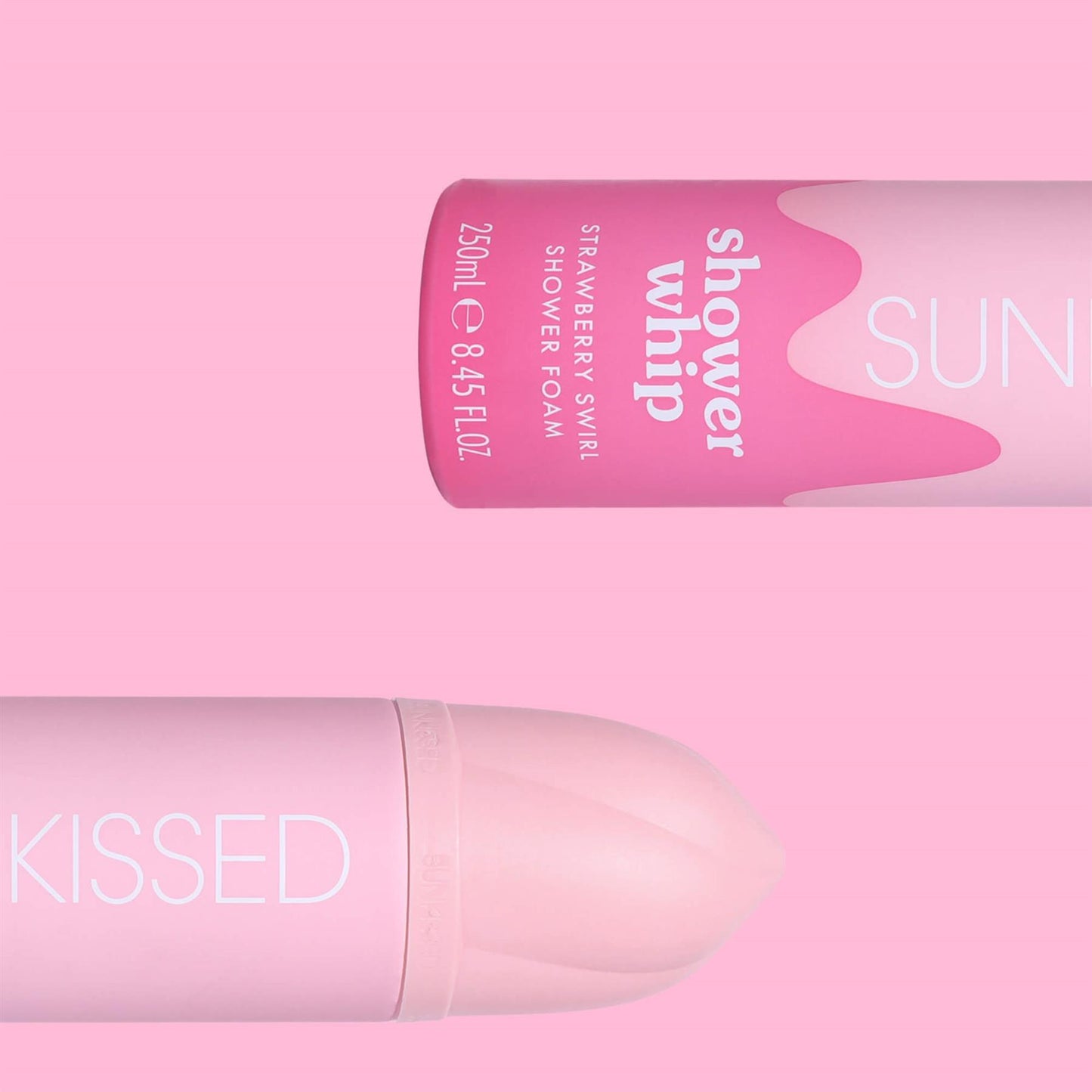 Close-up of two Sunkissed Strawberry Swirl Shower Whip bottles displayed horizontally against a vibrant pink background