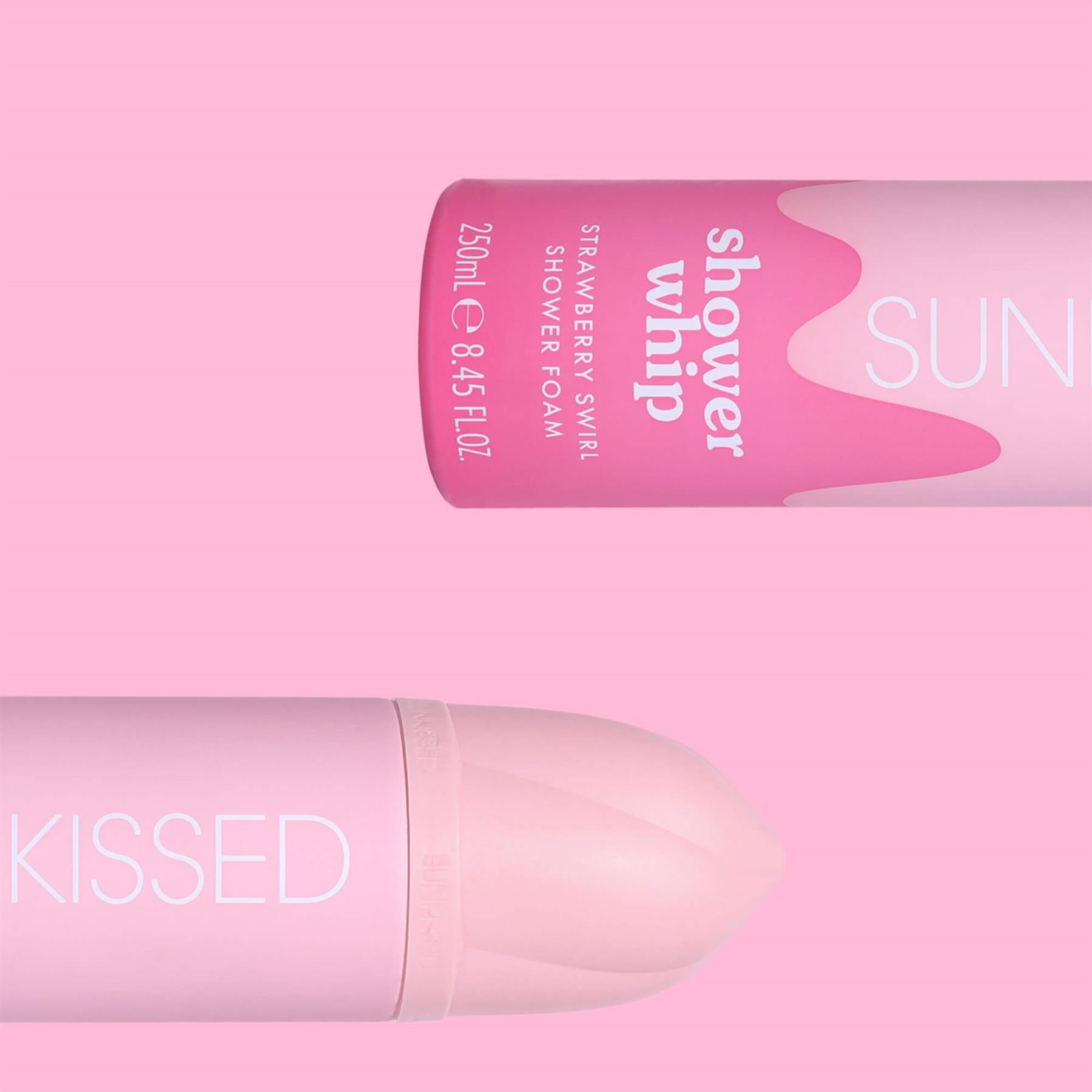 Close-up of two Sunkissed Strawberry Swirl Shower Whip bottles displayed horizontally against a vibrant pink background